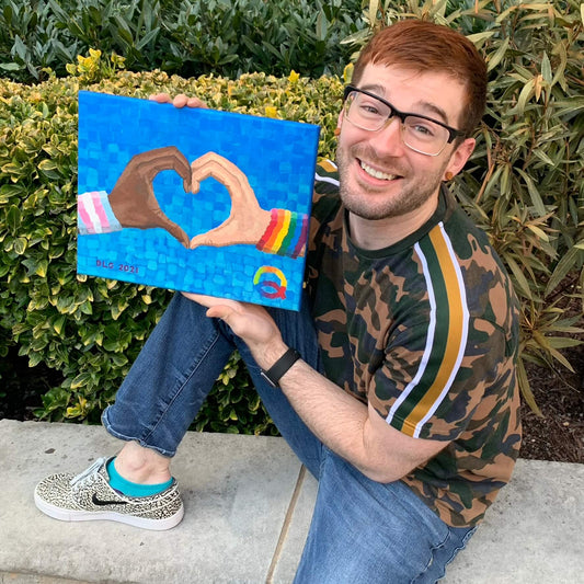 Dorrin Gingerich, a proud LGBTQ individual, holding the Loving Pride Art Print — a blue pride canvas print celebrating love, identity, and LGBTQ wall art expression.