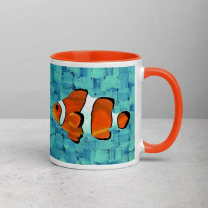 A ceramic mug with an orange rim and a vibrant hand-painted clownfish design on the side.