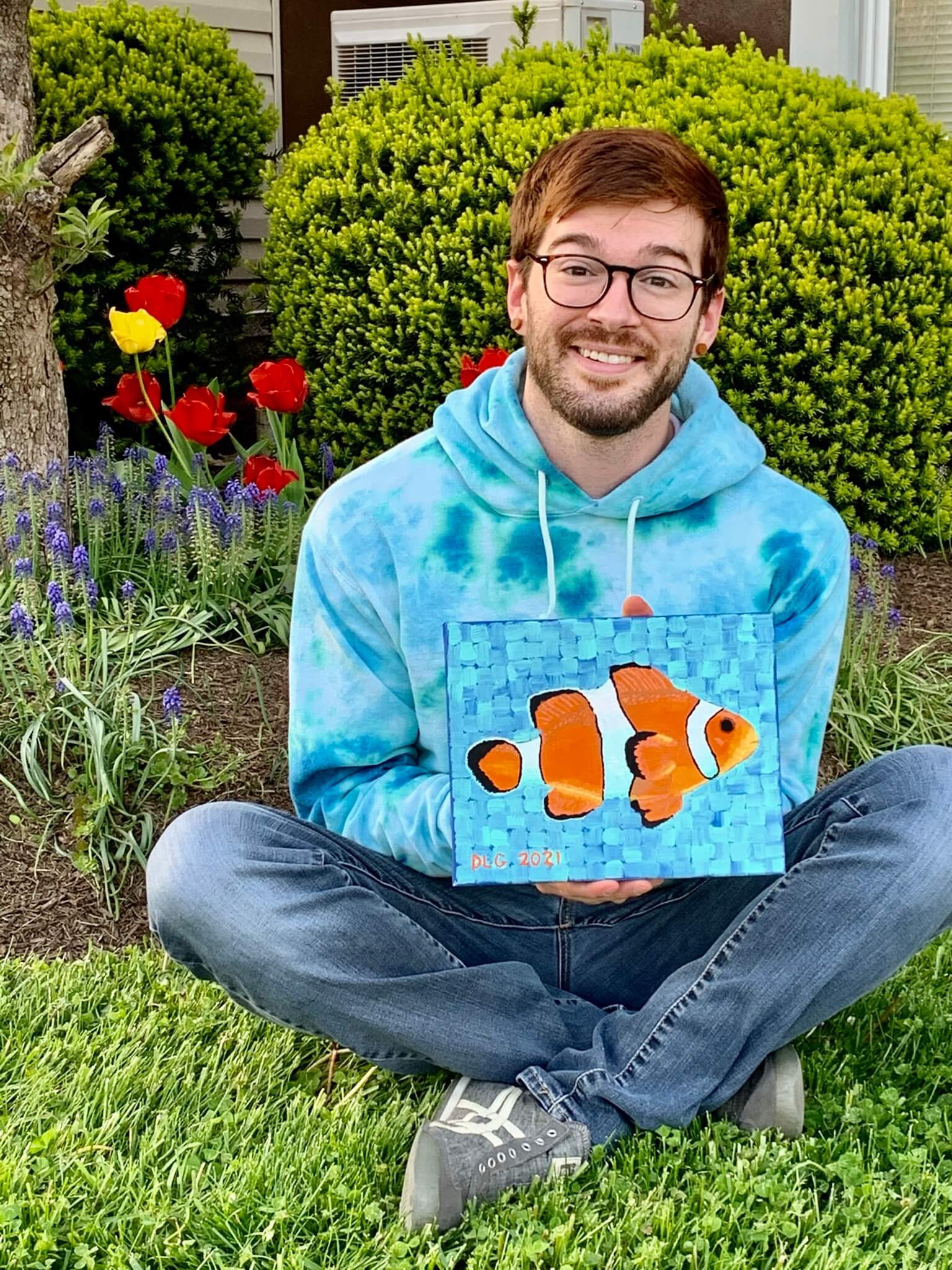 Dorrin Gingerich sitting on grass, gently holding a clownfish painting in his hands.