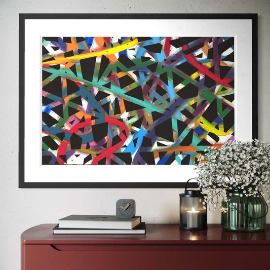 Framed abstract artwork with colorful lines on a wall above a wooden cabinet.