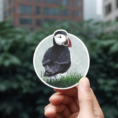 A person holding a sticker with a puffin bird on it, showcasing the adorable bird's vibrant colors and distinctive features.