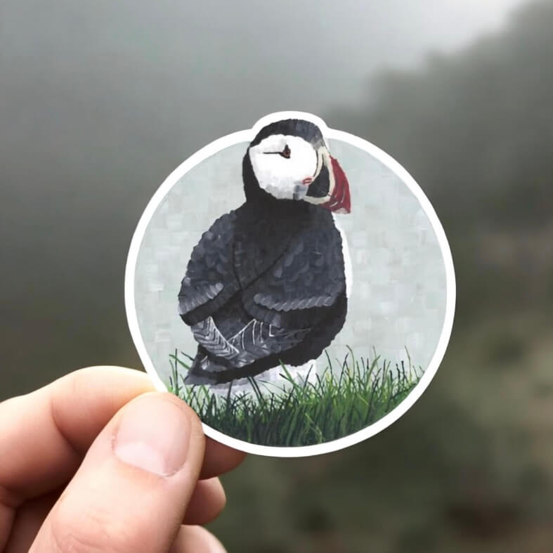 A person holding a sticker with a puffin bird on it, adding a touch of cuteness and nature to their belongings.