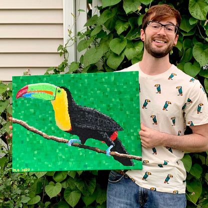 Artist Dorrin Gingerich holding his original toucan painting outdoors