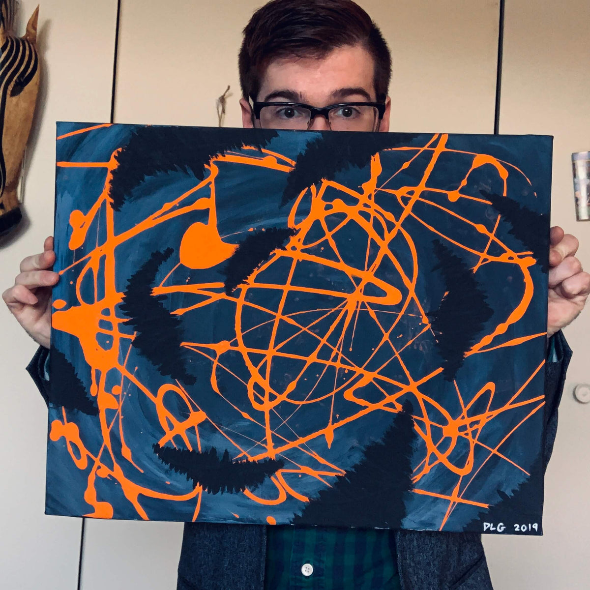Artist holding the original Darkness Conspires 1 painting with orange drips on blue canvas