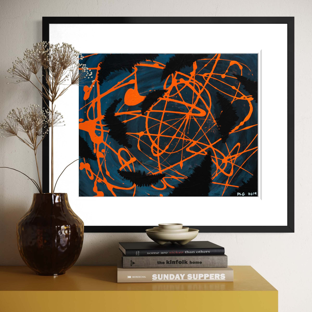 Darkness Conspires 1 framed above a credenza styled with dried flowers and design books