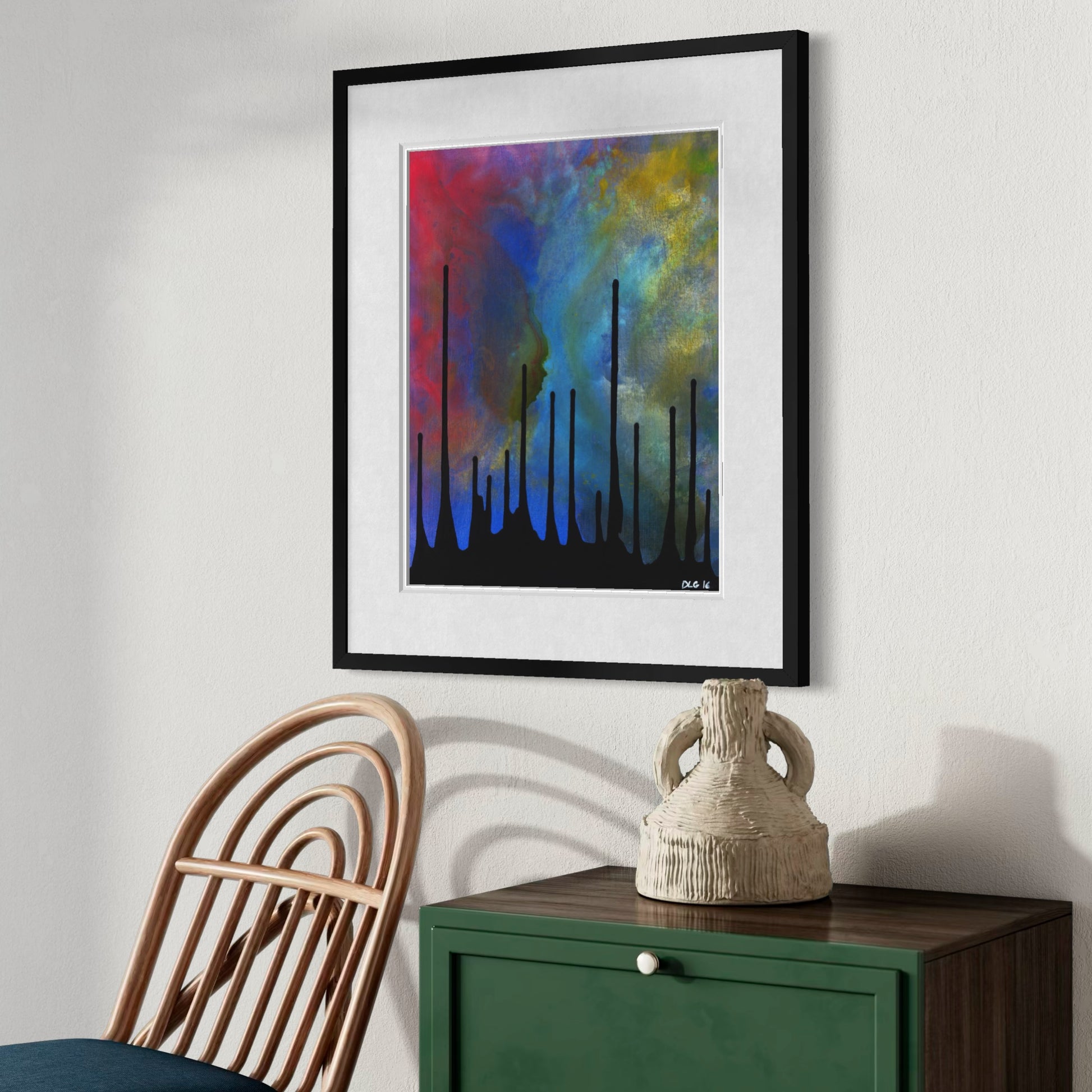 Angled view of the framed Drip print beside a rattan chair and pottery