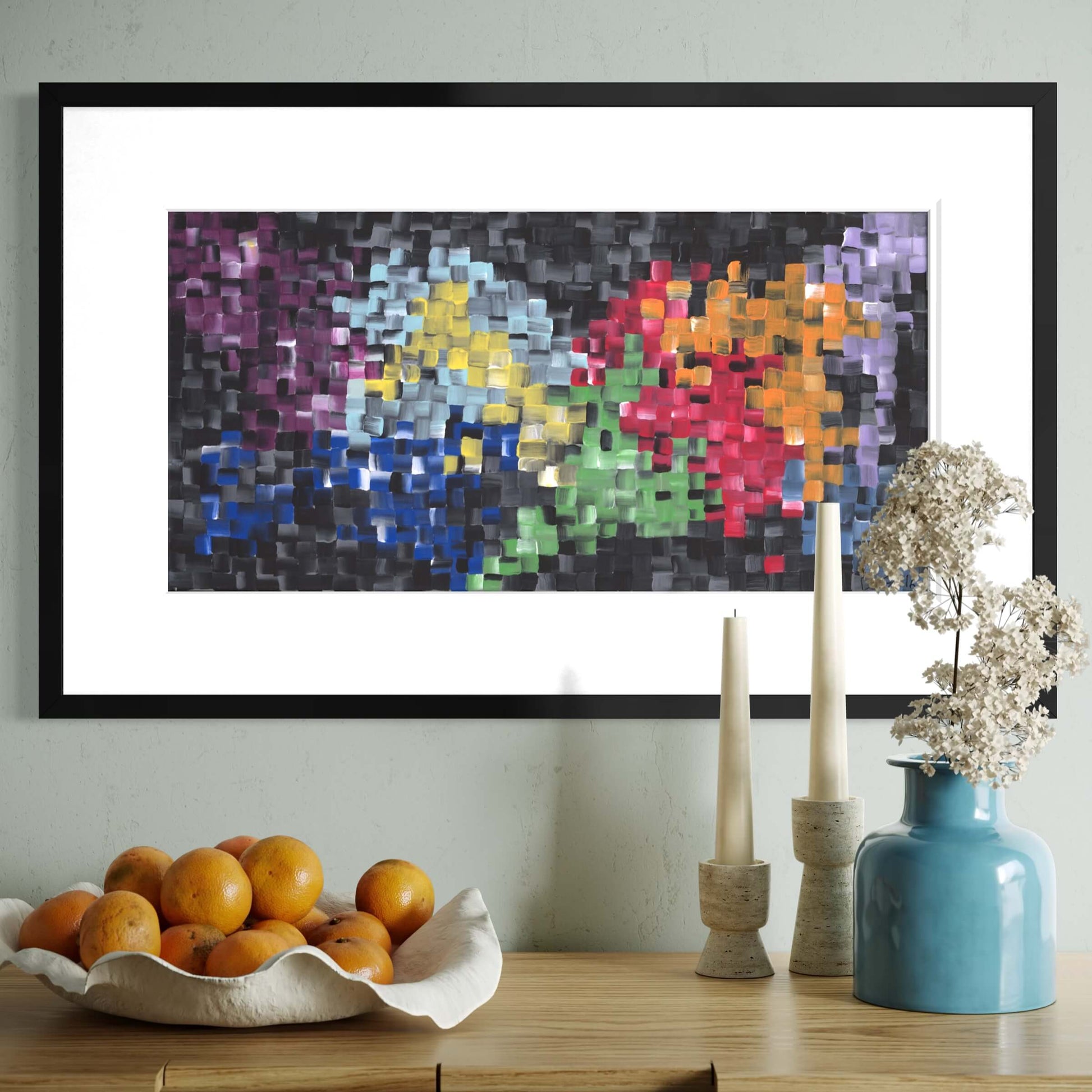Framed First art print above a console styled with oranges, candles, and a blue vase