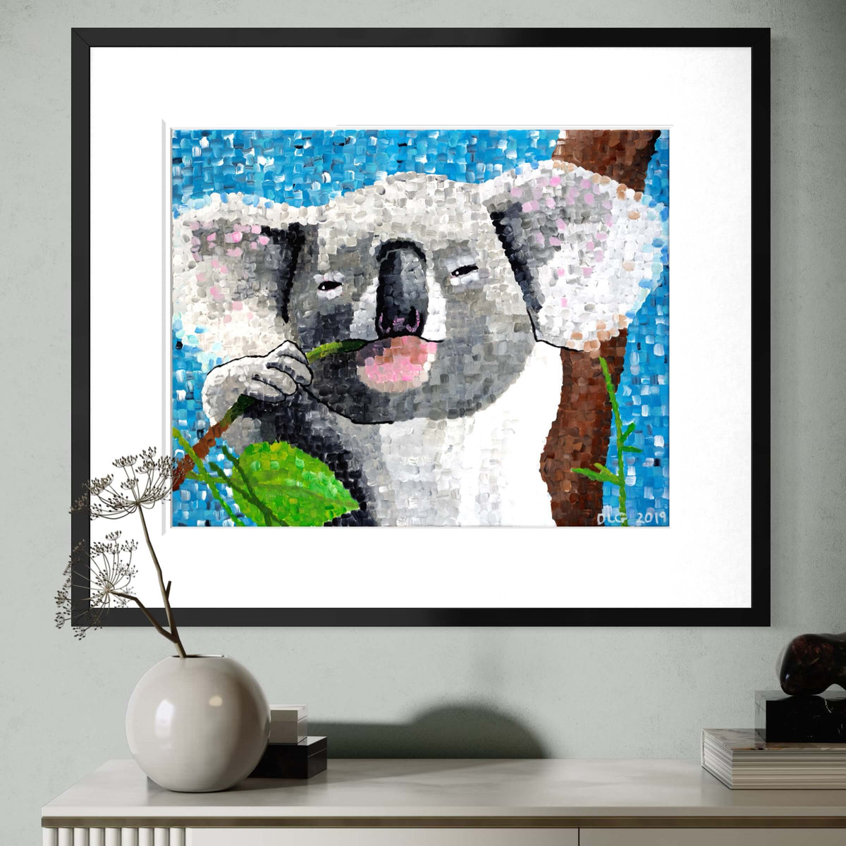 Koala wall art framed above a console with a vase and books in a living room