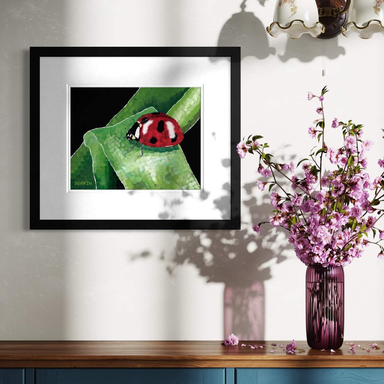 Ladybug painting framed on wall beside pink cherry blossom arrangement, nature art decor