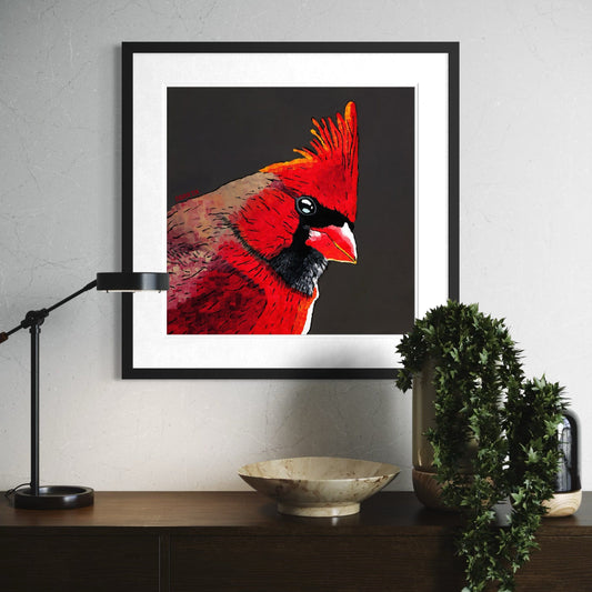Vibrant red cardinal bird art print with black background in white matted frame displayed above wooden console