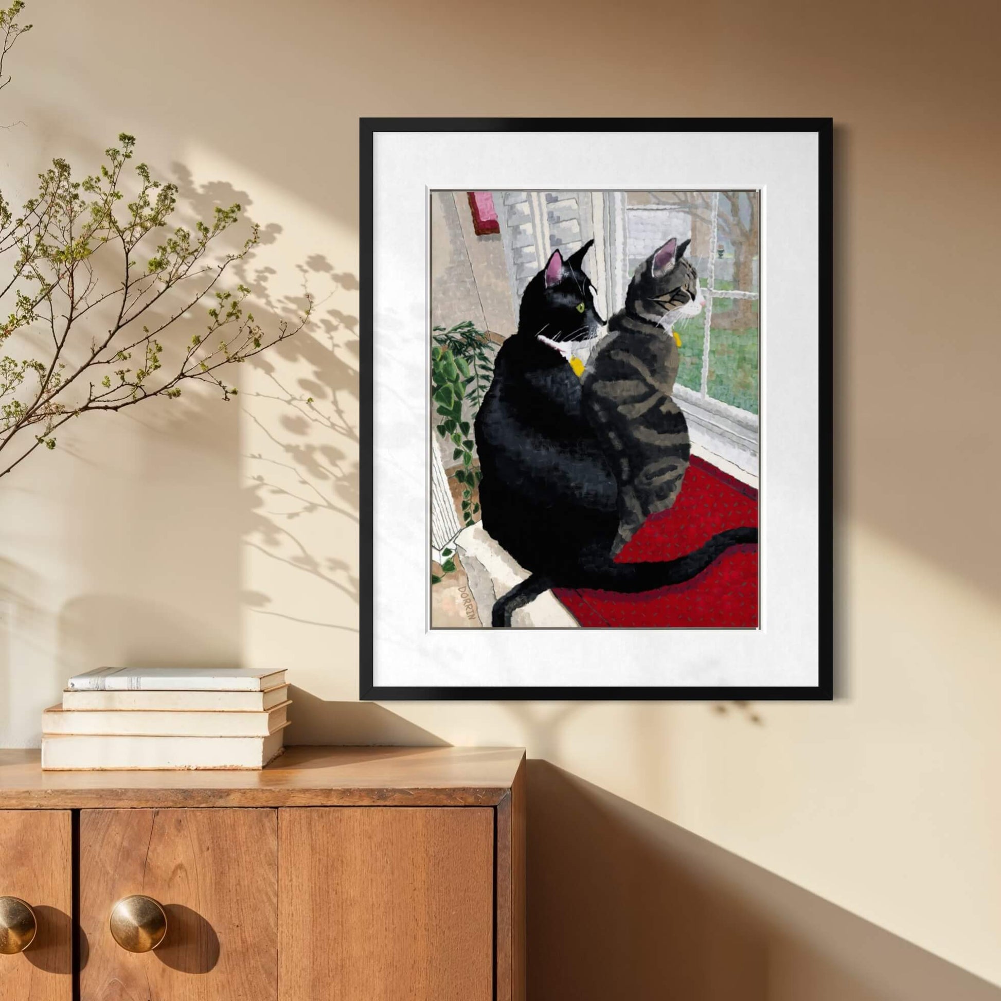 Framed cat print hanging above a wood console table in a sunlit entryway