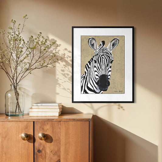 Framed zebra art print on a beige wall above a wood cabinet with books